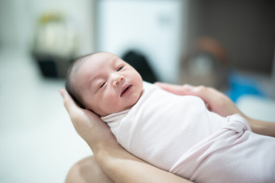 Close Up of Gentle Hands Supporting Awake Swaddled Newborn Baby Girl