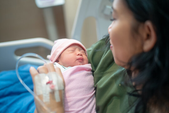 Happy Mother Holding Her Sleeping Newborn Baby Girl in Hospital Bed After Delivery