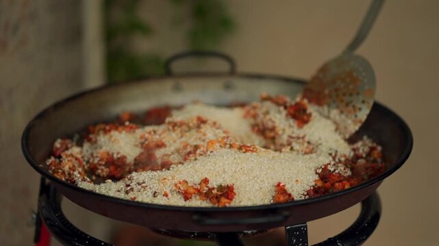 Chef mixing rice in a paella pan with a skimmer