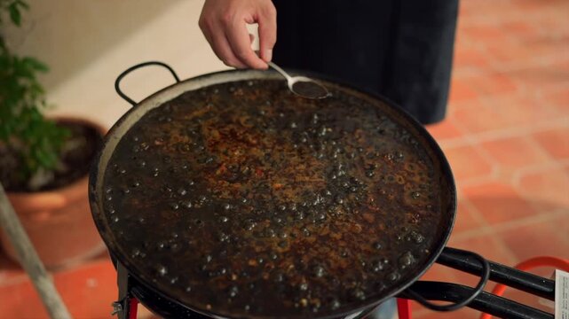Chef cooking black paella with squid ink outdoors