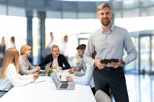 Smiling businessman manager executive standing in office with colleagues on the background