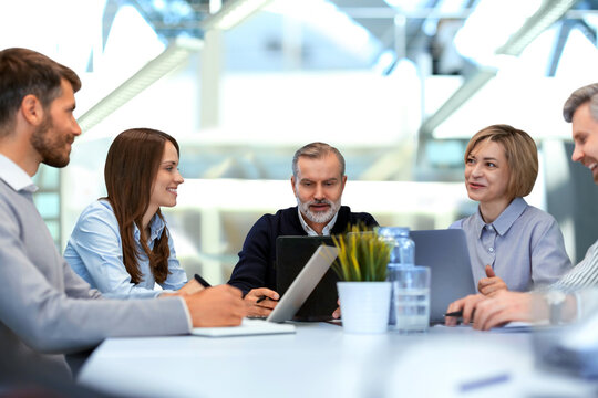 Five business people discussing work together using a tablet in a modern office
