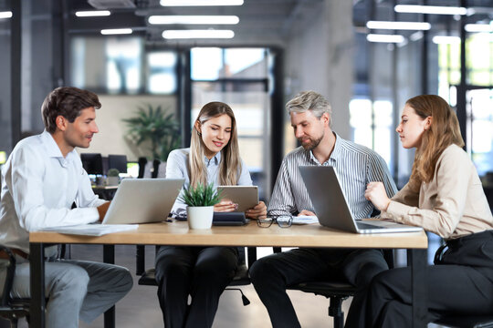 Successful businesspeople working in a coworking space working with laptop discussing strategy and business plan in modern office.