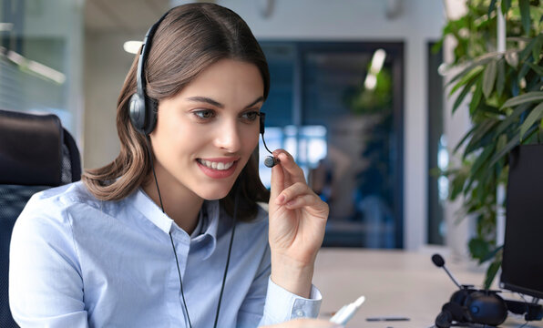 Female customer support operator with headset and smiling, with collegues at background.