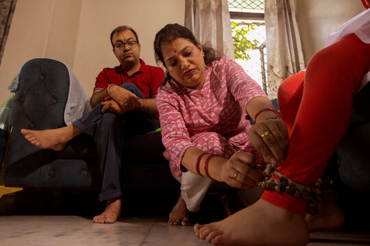 mother tying ghungroo on her daughter's ankle and father watching in background