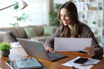 Fototapeta premium Happy teleworker comparing paper document online working at home