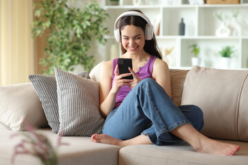 Obraz premium Happy teenage girl wearing headphone using smartphone at home