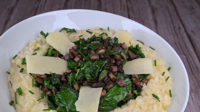 A bowl contains a serving of mushroom and spinach risotto. On top are pieces of Morteau sausage and parmesan cheese. The dish is placed on a wooden surface.