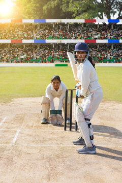 Female cricketer batting on a sunny day in a packed stadium