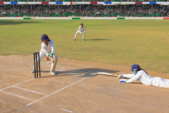 Wicketkeeper catching the ball as a cricketer dives to the crease
