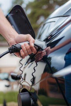Man holding power supply cable at electric vehicle charging station.