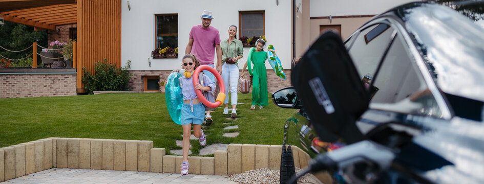 Happy family leaving home for summer vacation with luggage and pool toys.