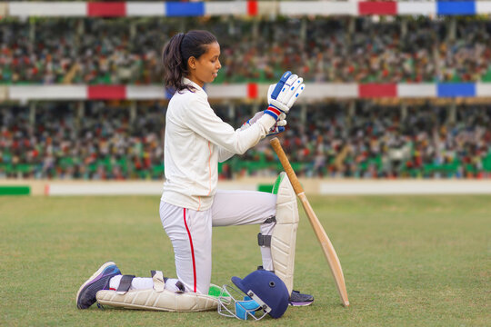 Female cricketer preparing on field with bat and gloves