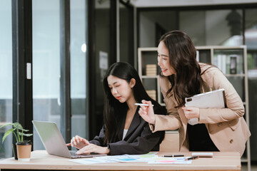 Fototapeta premium Two businesswomen reviewing financial reports and discussing strategy in a modern office, collaborating on data analysis, planning, and decision-making during a professional meeting.