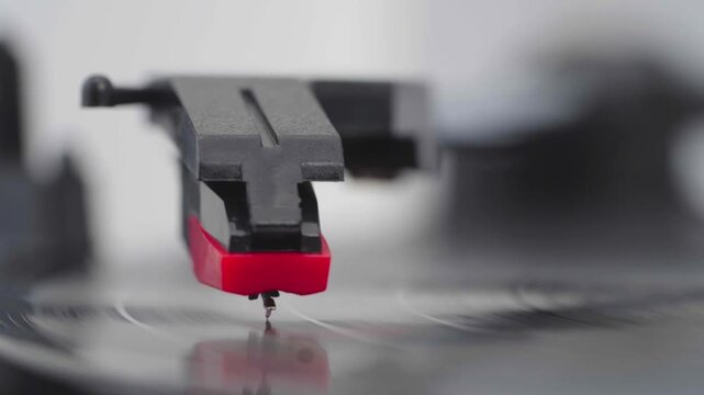 Red stylus glides over vinyl groove. Record spins beneath stylus with gentle precision. Focus sharp on needle contact with groove. Close-up captures analog music listening ritual