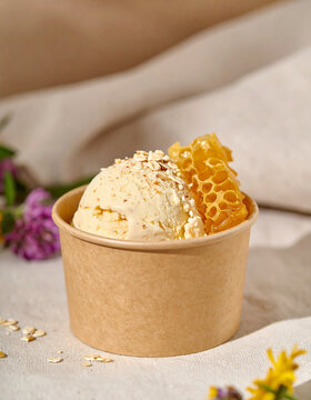 Creamy wild honey ice cream with organic rolled oats and small piece of honeycomb in kraft cup. Appetizing dessert. Tasty sweet food. Close-up.
