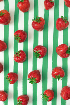 Fresh strawberries arranged  on a white background with green hand-painted vertical  stripes. 
