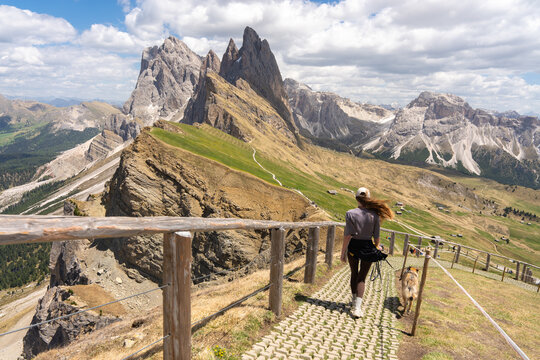 Young woman hiking with her dog on Seceda mountain trail in Italian Dolomites, active lifestyle adventure and scenic alpine summer landscape of Odle Geisler peaks