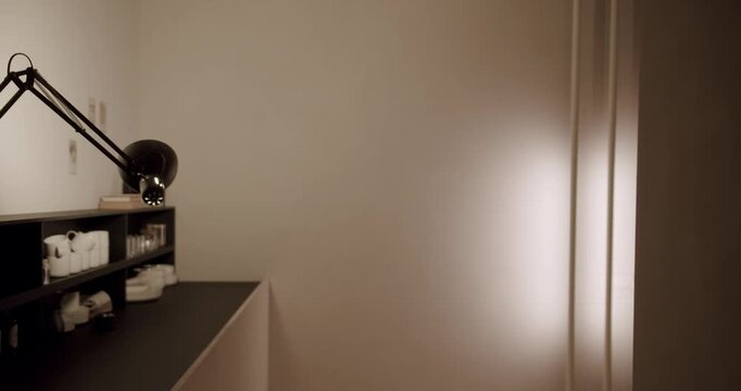 Modern office interior with a black desk, shelves, and an adjustable lamp. Soft, warm light illuminates the corner, creating a quiet and minimalist atmosphere perfect for concentration and work