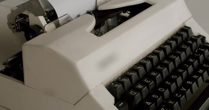 Close-up shot of an old white mechanical typewriter with black keys and a QWERTY keyboard layout, showing details of the classic writing machine in a slow and smooth camera movement
