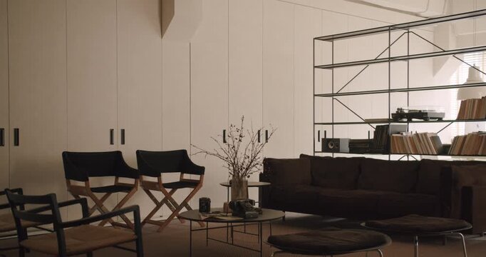 Minimalist and modern living room featuring a dark sofa, stylish chairs, and a metal shelving unit with a vinyl record player, creating a cozy and sophisticated atmosphere for comfortable living