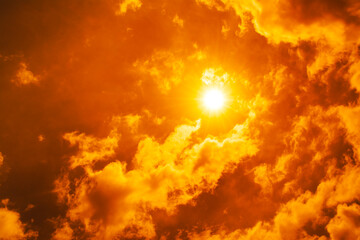Obraz premium Dramatic blazing sun shining through fiery orange clouds during an extreme heatwave, global boiling and climate crisis concept, hot summer weather background.