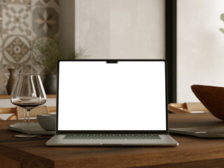 Fototapeta premium Laptop with empty white display on dining table with wine glass and decorative tile wall