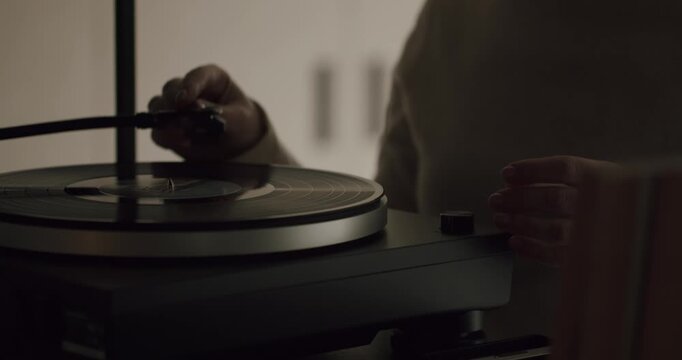 Close-up of a woman's hand carefully turning on a modern record player and placing the tonearm with the needle onto the spinning vinyl record, creating a nostalgic and relaxing atmosphere
