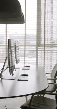 Modern and minimalist office interior with sleek black desks, chairs, and computers next to a large window with blinds, creating a calm and professional atmosphere, corporate work or study. vertical