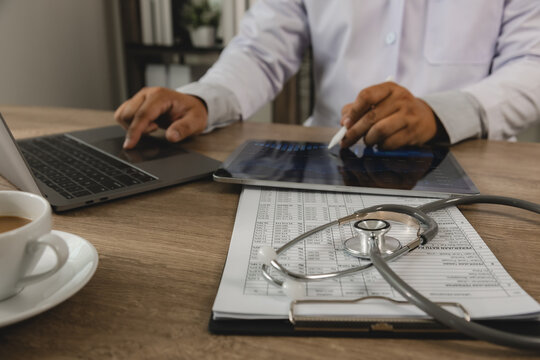 Healthcare business intelligence professional analyzing data dashboard on tablet and laptop with medical records. KPI monitoring, healthcare analytics, performance reporting, digital transformation an