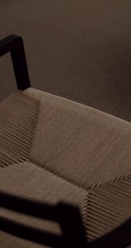 Detailed close-up shot revealing the intricate texture of a brown woven chair seat, with shadows moving slowly across the surface, highlighting the craftsmanship and natural fiber material. vertical