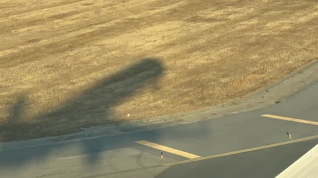 Left side cockpit view of the elongated shadow of a jet airplane on the ground during a real time landing with an early morning light.