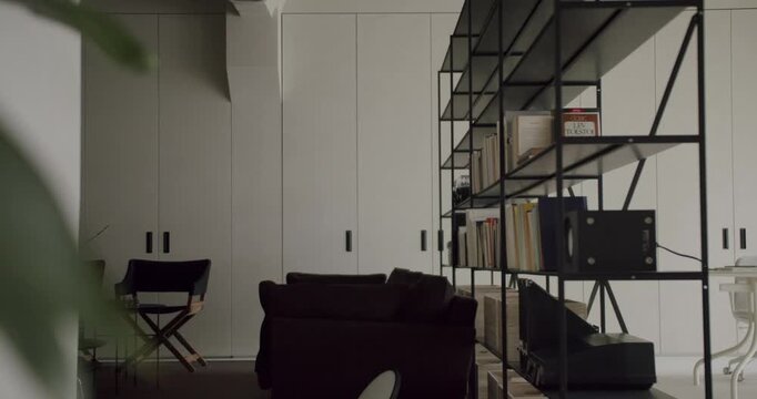 Minimalist living room interior featuring a contemporary black metal bookshelf, a cozy dark armchair, and sleek white built-in wardrobes, creating a stylish and tranquil living space