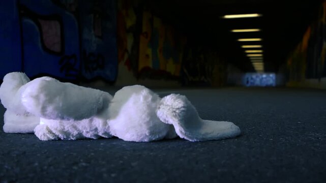 Lost and forgotten white stuffed bunny rabbit lying on the asphalt ground of a dark, graffiti covered pedestrian underpass, symbolizing loneliness, neglect, and lost childhood innocence