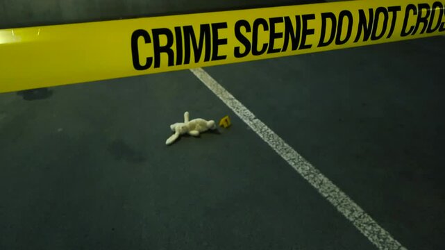 Yellow police tape reading 'Crime Scene Do Not Cross' moving to reveal a toy bunny lying on the ground next to a numbered evidence marker inside a dark underground parking garage