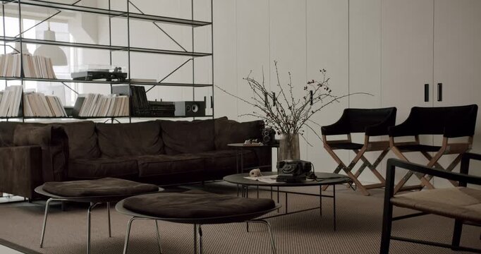 Stylish and contemporary living room featuring a comfortable brown suede sofa, sleek metal shelving with books and a record player, and a central coffee table with a vintage telephone
