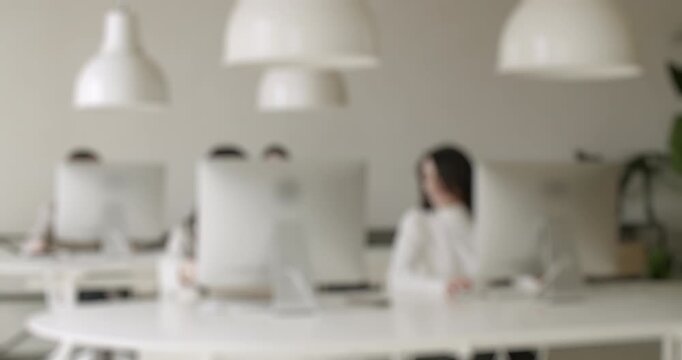 Defocused shot of a modern and bright open-plan office with employees working at computers, creating a neutral and professional background for corporate concepts and business presentations