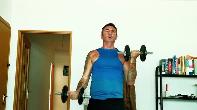 A man trains using dumbbells to stress his biceps. The video is a typical example of staying fit by working out at home