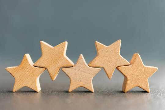 Five wooden stars in a row on grey background. Concept of five star hotel rating, premium quality service, top business review, customer satisfaction and excellent classification.