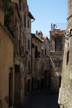 Vicolo antico di un borgo europeo con edifici in pietra, facciate vissute e dettagli architettonici tradizionali, illuminato dalla luce naturale che esalta l&rsquo;atmosfera pittoresca e senza tempo del luo