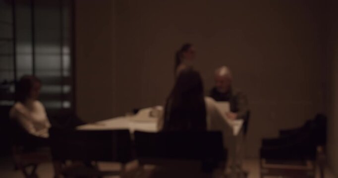 Out of focus view of business people sitting around a table during a tense and mysterious corporate meeting or group therapy session, creating an anonymous and dramatic atmosphere in slow motion