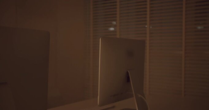 Warm cinematic light illuminating an empty modern office space at night, revealing rows of unoccupied workstations and computers, creating a serene and quiet atmosphere after working hours
