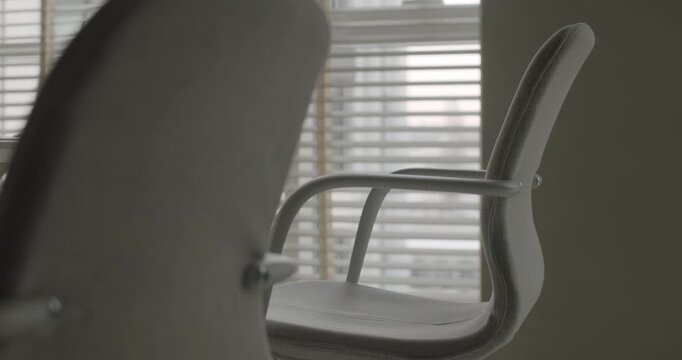 Empty white modern office chair slowly turning in a bright contemporary workspace with a window and blinds in the background, symbolizing a vacant position, waiting, or loneliness