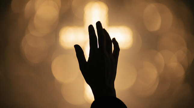 Woman raising hand toward glowing cross in dark room. Christian worship and prayer service. Easter celebration, religious faith and spiritual devotion concept. Light in darkness