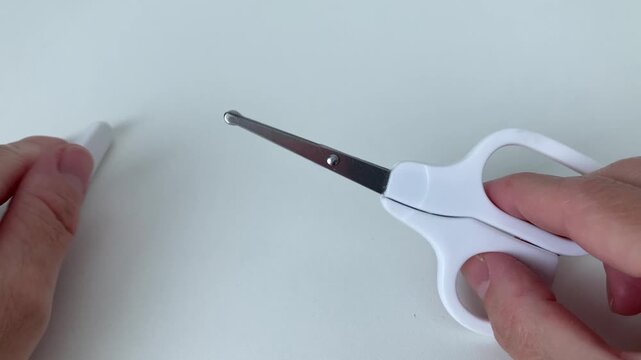 A woman removes the protective cap from a pair of baby scissors. Close-up of a woman's hands with scissors on a white background. The rounded ends of the blades protect against cuts and injuries