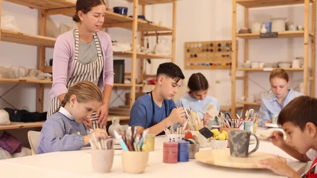 Pleased underage attendees of pottery circle color handmade work-pieces with female instructor