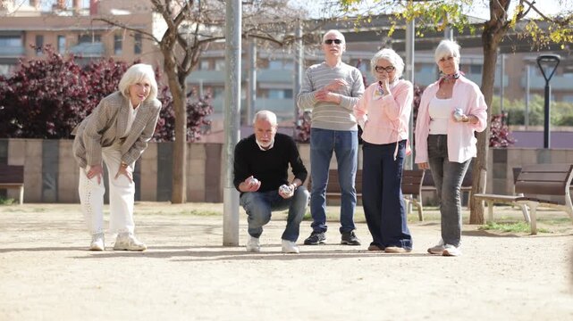  Elderly men and women playing petanque together in a courtyard, throwing metal balls
