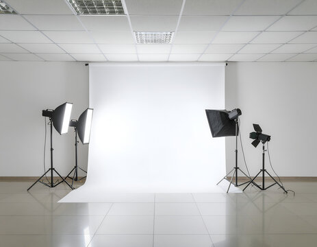 A bright, minimalist photography studio setup features two lighting rigs illuminating a seamless white backdrop against a clean, white-walled interior.