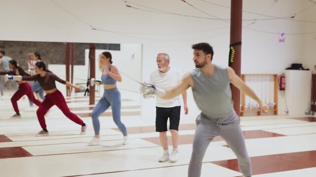 Group of men and women fencers practice epee techniques individually in sports hall