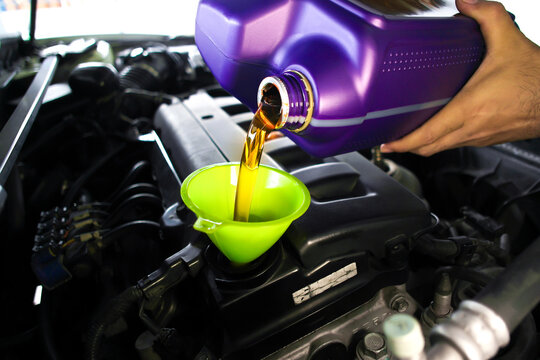 Pouring fresh synthetic motor oil from a purple container into a car engine using a bright green funnel during routine vehicle maintenance